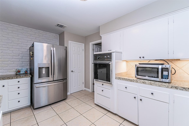 kitchen featuring appliances with stainless steel finishes, tasteful backsplash, light stone counters, light tile patterned floors, and white cabinets