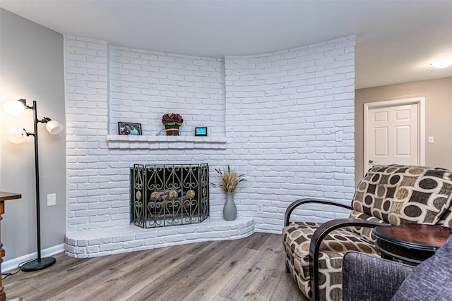 living area featuring a fireplace, brick wall, and hardwood / wood-style flooring