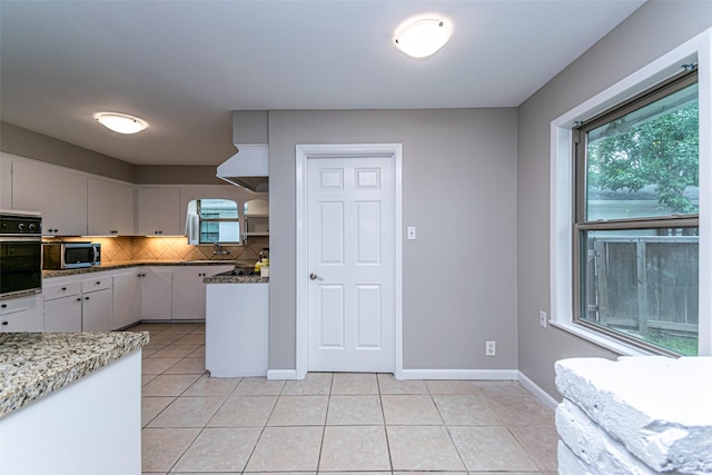 kitchen featuring white cabinets, backsplash, oven, and light tile patterned flooring