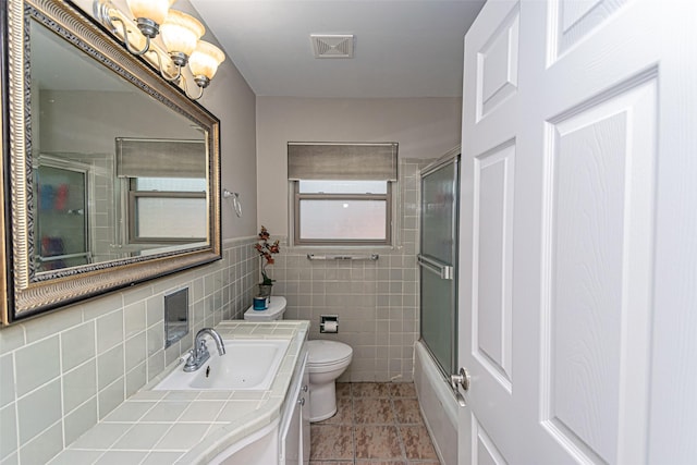 full bathroom with vanity, combined bath / shower with glass door, tile walls, and toilet