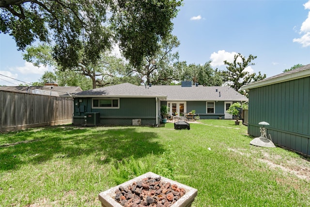 rear view of property featuring cooling unit, an outdoor fire pit, and a lawn