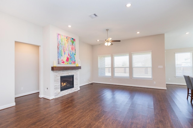 unfurnished living room featuring ceiling fan, dark hardwood / wood-style floors, and a stone fireplace