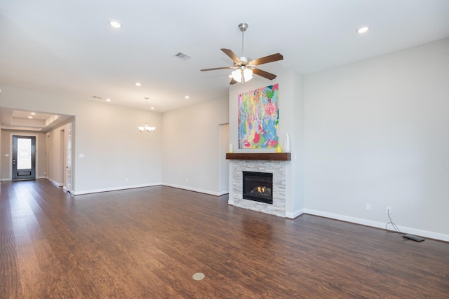 unfurnished living room featuring dark hardwood / wood-style flooring, ceiling fan with notable chandelier, and a stone fireplace