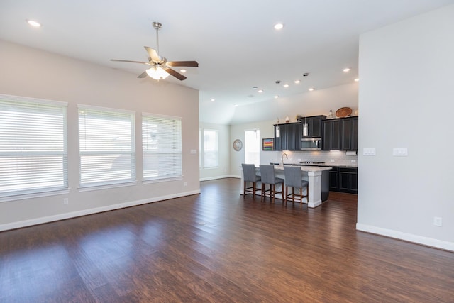 kitchen featuring lofted ceiling, backsplash, ceiling fan, a breakfast bar, and a center island with sink