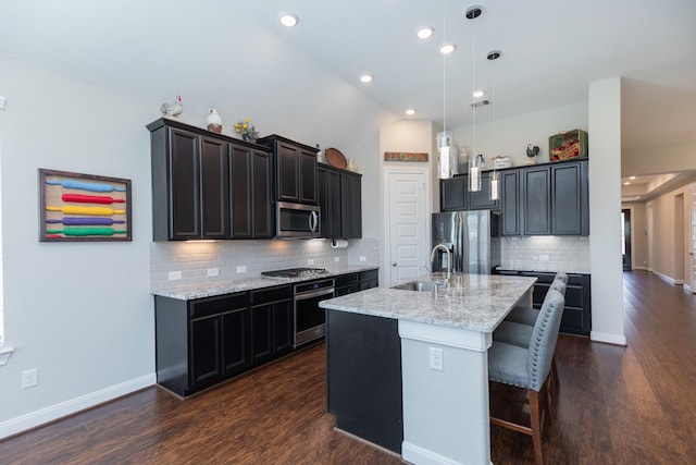 kitchen with light stone countertops, appliances with stainless steel finishes, decorative light fixtures, a kitchen bar, and an island with sink