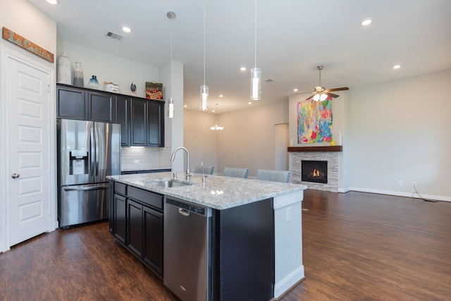 kitchen with ceiling fan, decorative backsplash, sink, appliances with stainless steel finishes, and an island with sink