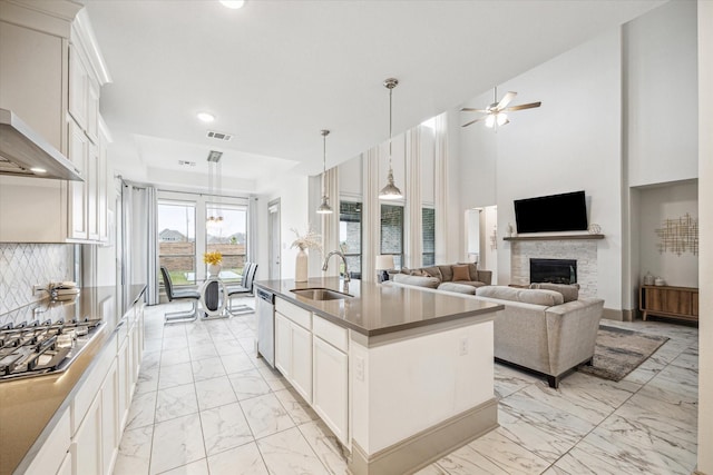 kitchen with a center island with sink, wall chimney range hood, sink, ceiling fan, and white cabinetry