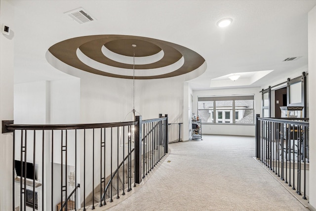 corridor featuring carpet, a barn door, and a raised ceiling