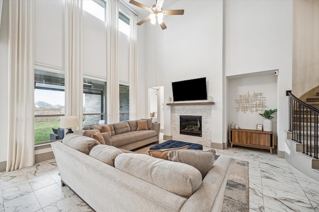 living room with a stone fireplace, ceiling fan, and a high ceiling