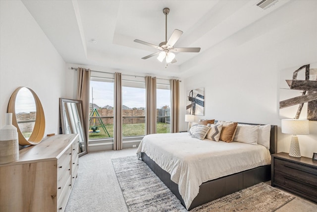 bedroom with light carpet, a raised ceiling, and ceiling fan