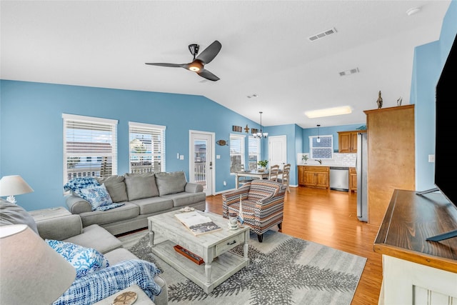 living room featuring light hardwood / wood-style floors, vaulted ceiling, ceiling fan with notable chandelier, and sink