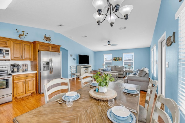 dining space featuring ceiling fan with notable chandelier, light hardwood / wood-style floors, and vaulted ceiling