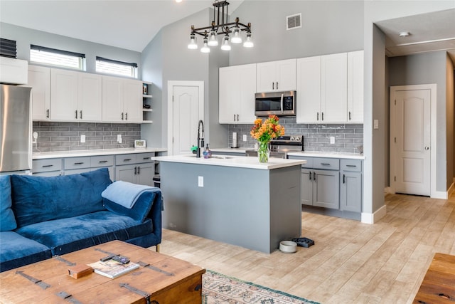 kitchen featuring pendant lighting, gray cabinetry, high vaulted ceiling, sink, and appliances with stainless steel finishes