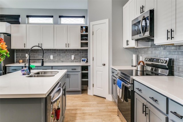 kitchen with gray cabinetry, sink, stainless steel appliances, decorative backsplash, and light wood-type flooring