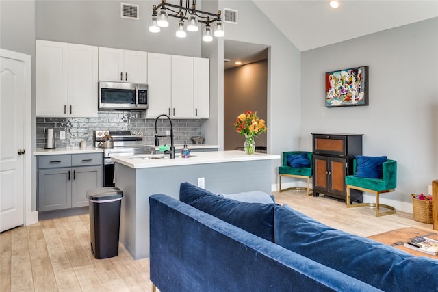 kitchen with gray cabinetry, an island with sink, pendant lighting, appliances with stainless steel finishes, and light wood-type flooring