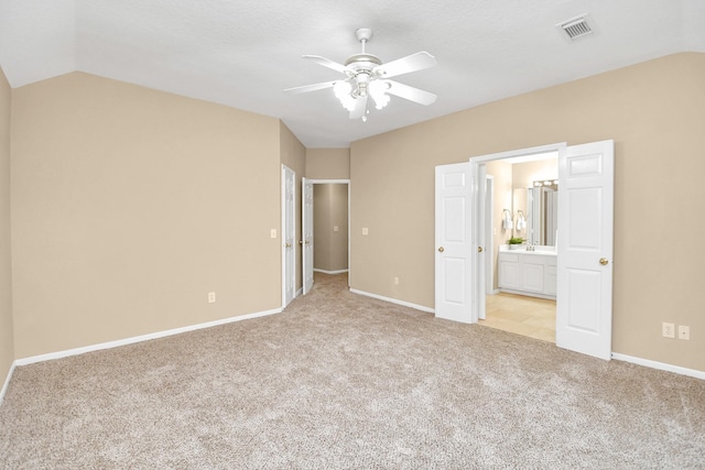 unfurnished bedroom with ceiling fan, light colored carpet, lofted ceiling, and ensuite bath