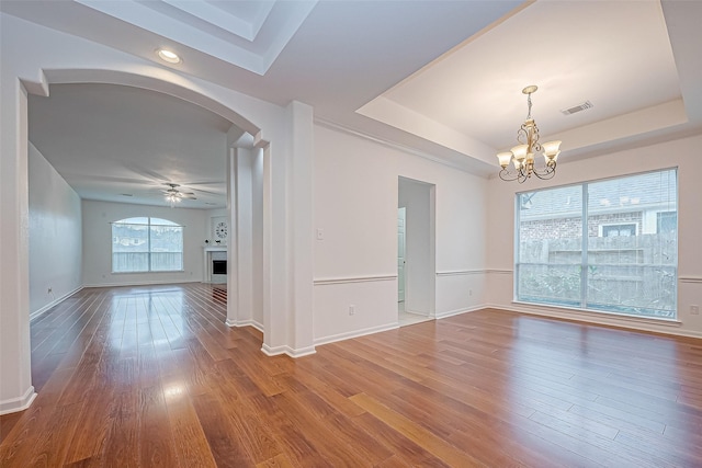 spare room featuring wood-type flooring, ceiling fan with notable chandelier, and a tray ceiling