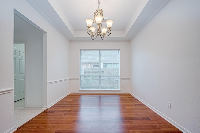 empty room with a raised ceiling, wood-type flooring, and an inviting chandelier