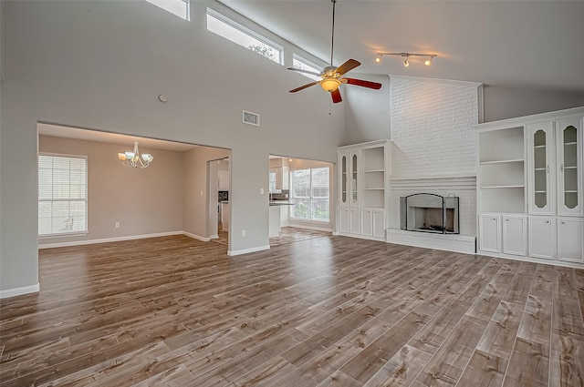 unfurnished living room featuring hardwood / wood-style floors, ceiling fan with notable chandelier, high vaulted ceiling, and a brick fireplace