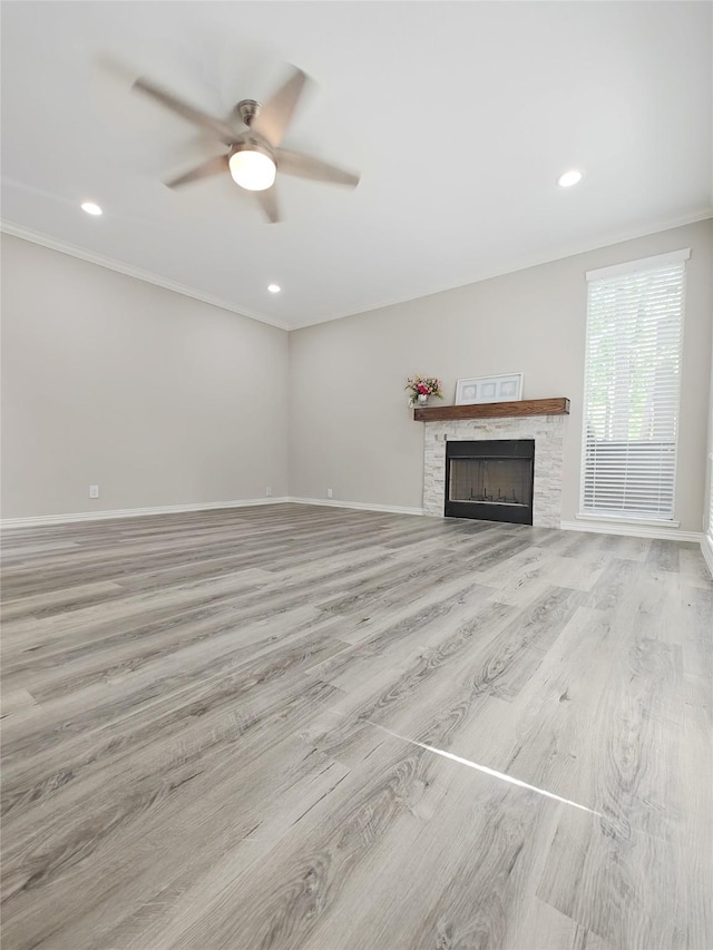 unfurnished living room featuring ceiling fan, a stone fireplace, light wood-type flooring, and ornamental molding