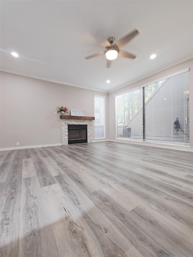 unfurnished living room with ornamental molding, light hardwood / wood-style flooring, ceiling fan, and a stone fireplace