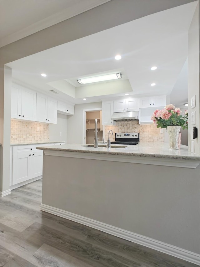 kitchen featuring light stone countertops, light wood-type flooring, a raised ceiling, white cabinetry, and stainless steel electric range