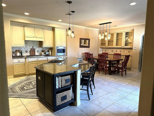 kitchen with appliances with stainless steel finishes, tasteful backsplash, dark stone countertops, hanging light fixtures, and an island with sink