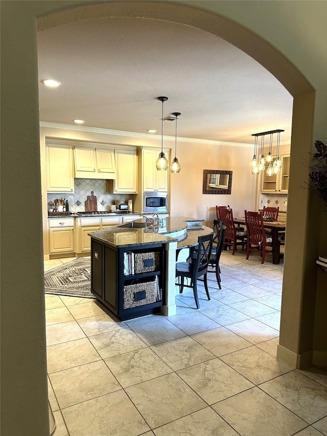 kitchen featuring a center island with sink, stainless steel appliances, decorative light fixtures, and ornamental molding