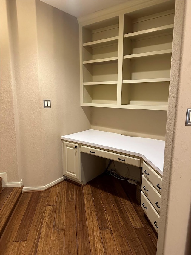 unfurnished office featuring dark hardwood / wood-style flooring and built in desk