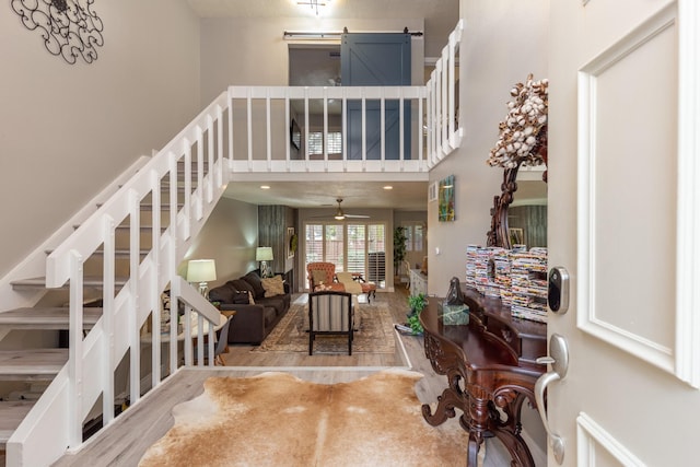 staircase featuring hardwood / wood-style floors, a towering ceiling, ceiling fan, and a barn door