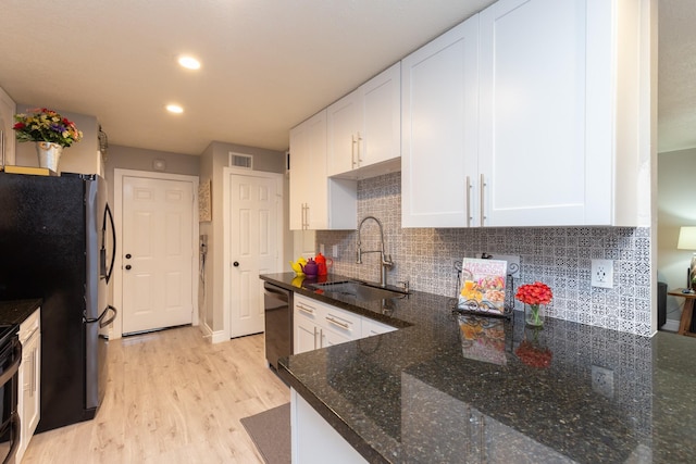 kitchen featuring stainless steel appliances, backsplash, white cabinets, dark stone counters, and sink