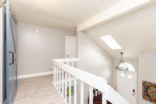 hall featuring a textured ceiling, light hardwood / wood-style flooring, and lofted ceiling with skylight