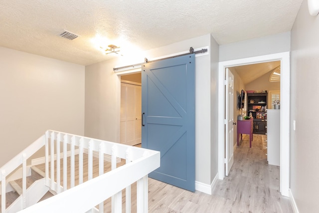 hall featuring a textured ceiling, a barn door, and light hardwood / wood-style flooring