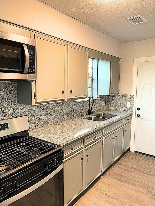 kitchen with sink, stainless steel appliances, light hardwood / wood-style flooring, a textured ceiling, and decorative backsplash