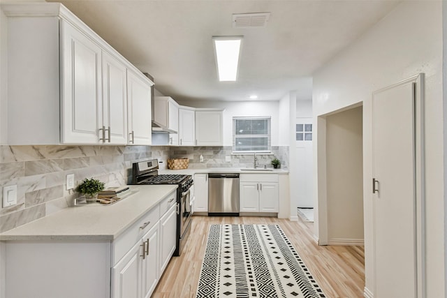 kitchen with white cabinets, appliances with stainless steel finishes, light hardwood / wood-style floors, and sink