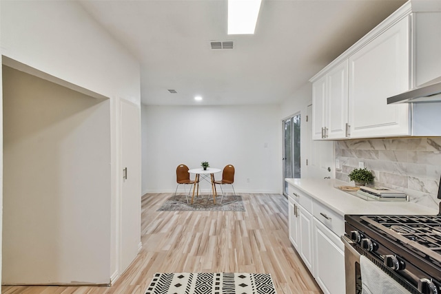 kitchen featuring white cabinets, stainless steel range with gas cooktop, decorative backsplash, wall chimney exhaust hood, and light hardwood / wood-style floors