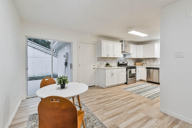 kitchen with wall chimney exhaust hood, stainless steel appliances, decorative backsplash, white cabinets, and light wood-type flooring