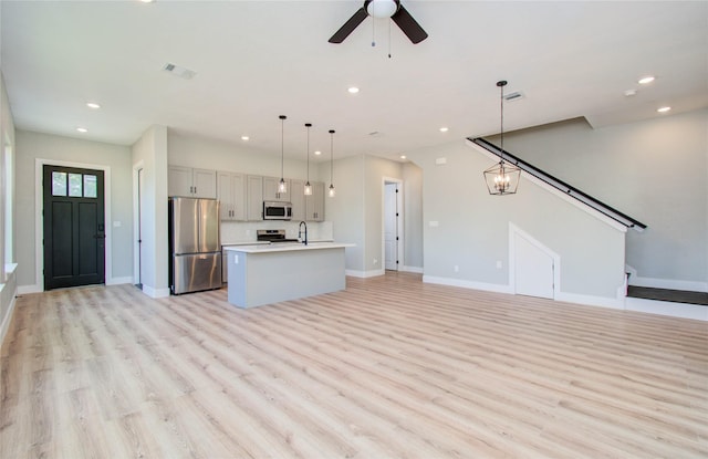 unfurnished living room with ceiling fan with notable chandelier, light wood-type flooring, and sink