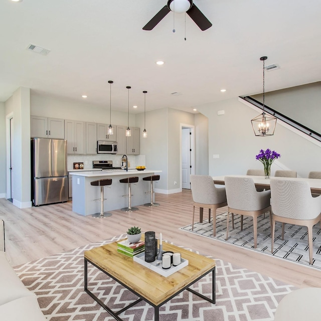 living room with ceiling fan with notable chandelier, light hardwood / wood-style floors, and sink