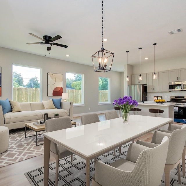 dining room with ceiling fan with notable chandelier, light wood-type flooring, and sink