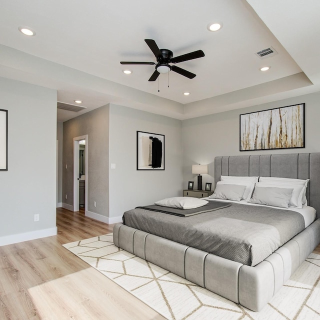 bedroom featuring light hardwood / wood-style floors, ceiling fan, and a tray ceiling