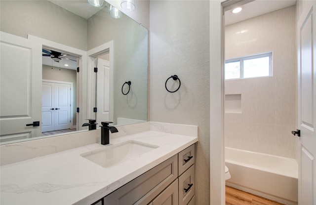 full bathroom with vanity, hardwood / wood-style flooring, ceiling fan, tiled shower / bath combo, and toilet