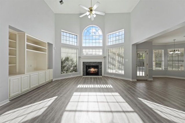 unfurnished living room featuring a wealth of natural light, a towering ceiling, dark wood-type flooring, and ceiling fan with notable chandelier