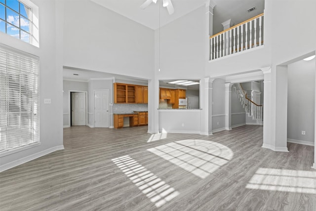 unfurnished living room featuring decorative columns, ceiling fan, light hardwood / wood-style flooring, and a towering ceiling