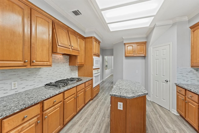 kitchen featuring light stone countertops, white appliances, a kitchen island, and crown molding