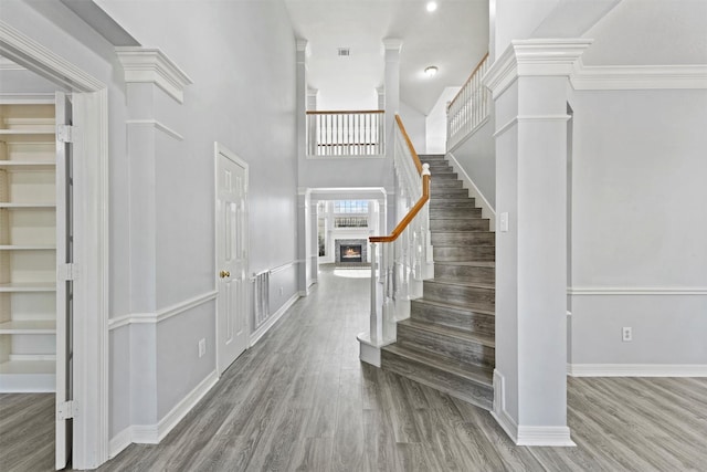 foyer entrance with hardwood / wood-style flooring, crown molding, a high ceiling, and decorative columns