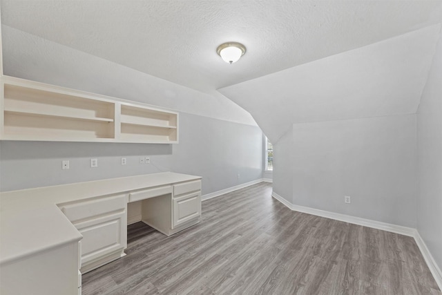 unfurnished office with light wood-type flooring, a textured ceiling, and vaulted ceiling