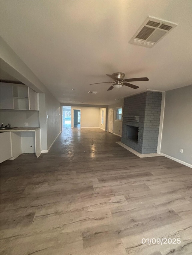 unfurnished living room with ceiling fan, a fireplace, sink, and hardwood / wood-style flooring