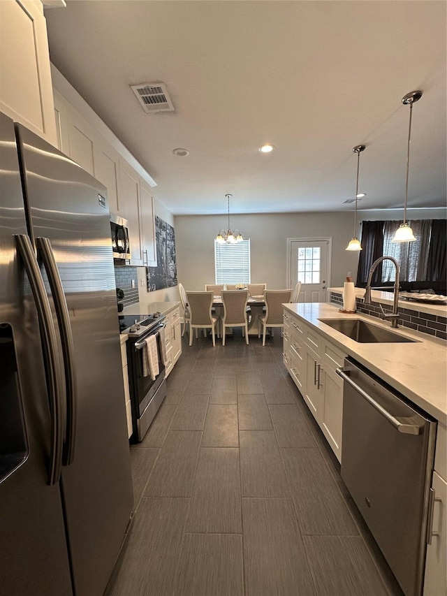 kitchen featuring appliances with stainless steel finishes, white cabinetry, pendant lighting, and sink