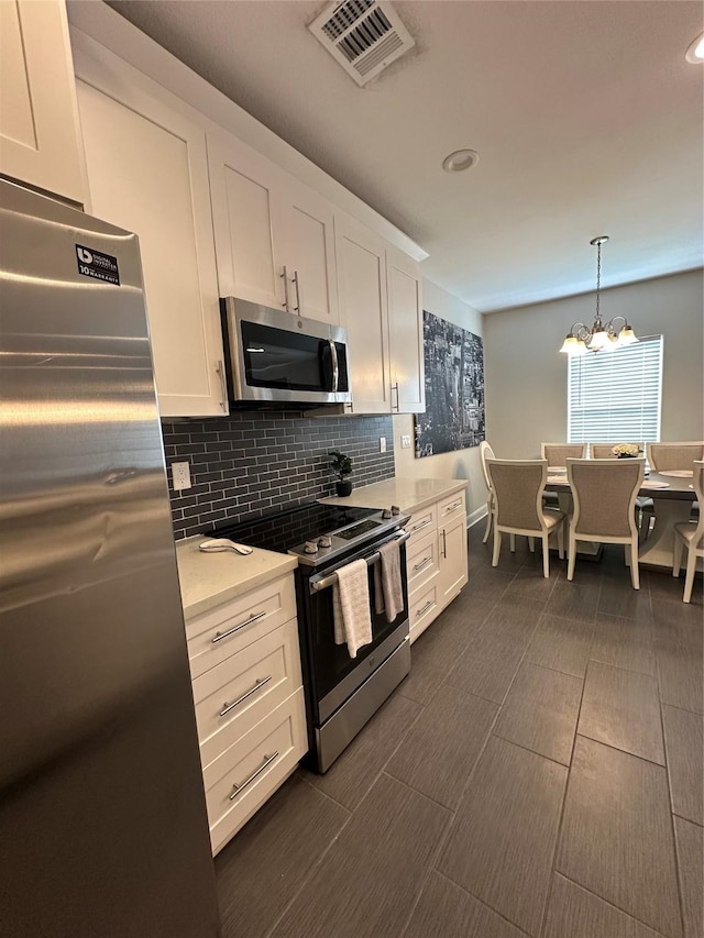 kitchen with white cabinets, stainless steel appliances, decorative light fixtures, and a notable chandelier